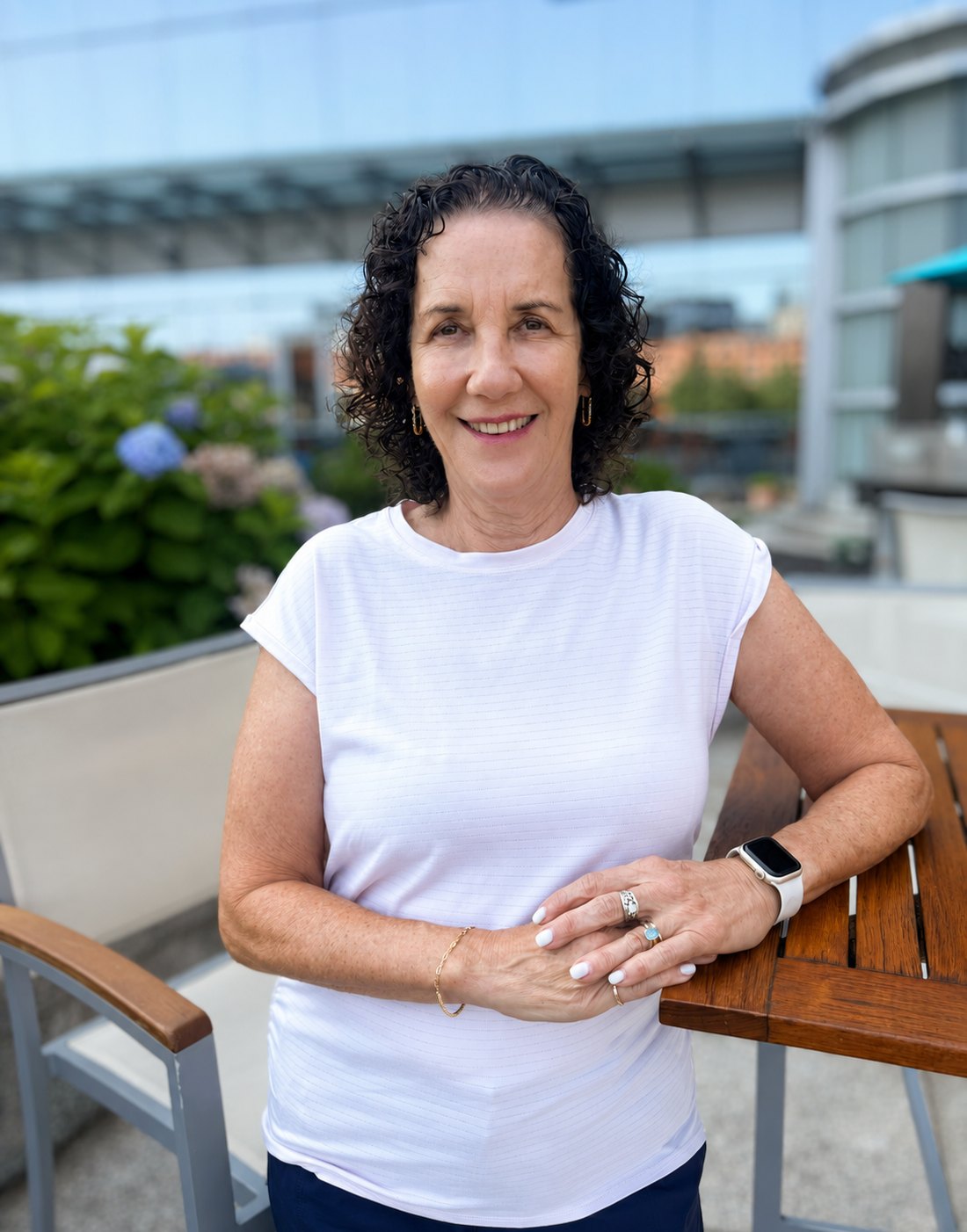 Marsha Gallinger smiling outdoors on a rooftop terrace, wearing a white top